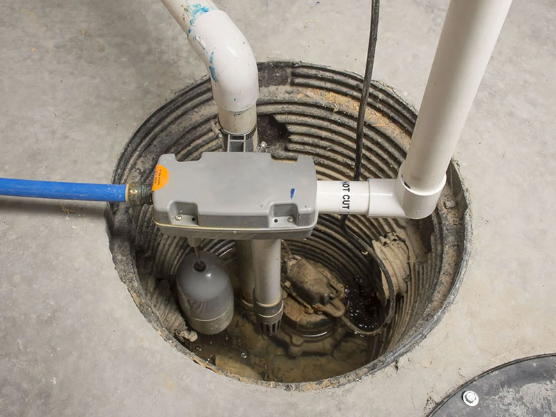 Close-up view of a sump pump installed in a basement with pipes and electrical cords connected.